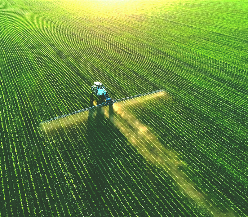 Traktor besprutar ett grönt fält, sett från ovan